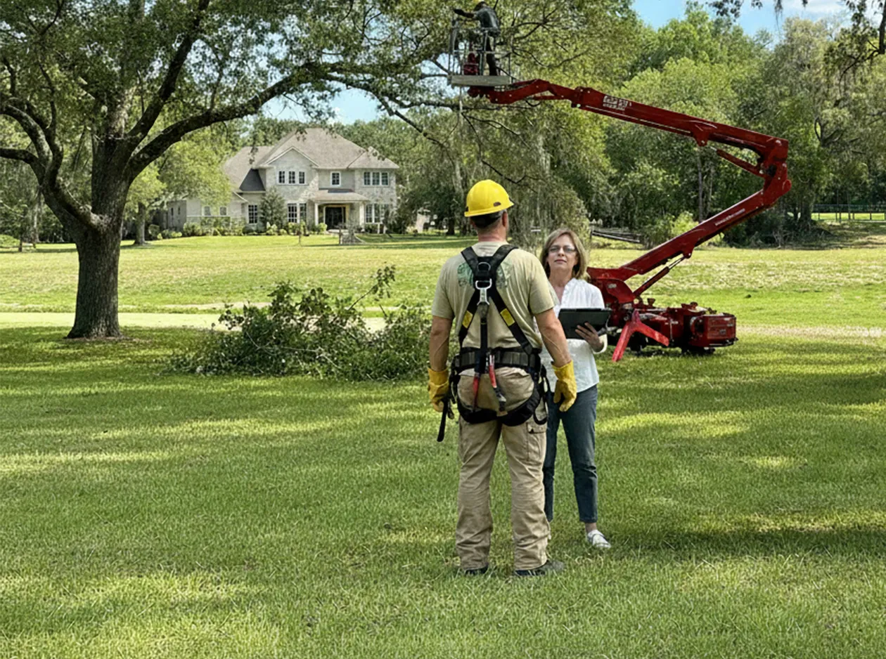 Arborist and homeowner discussing tree trimming in a spacious, well-maintained yard with a lift.