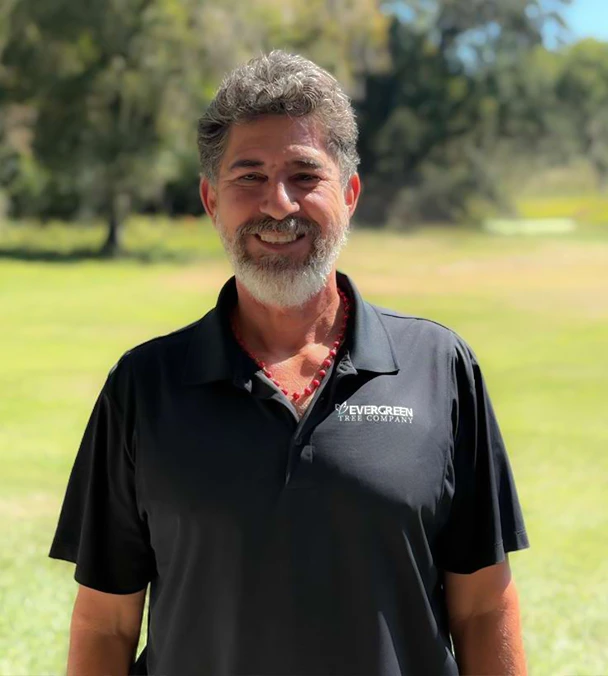 Carlos Castillo, founder of Evergreen Tree Company, standing outdoors in a green landscape.